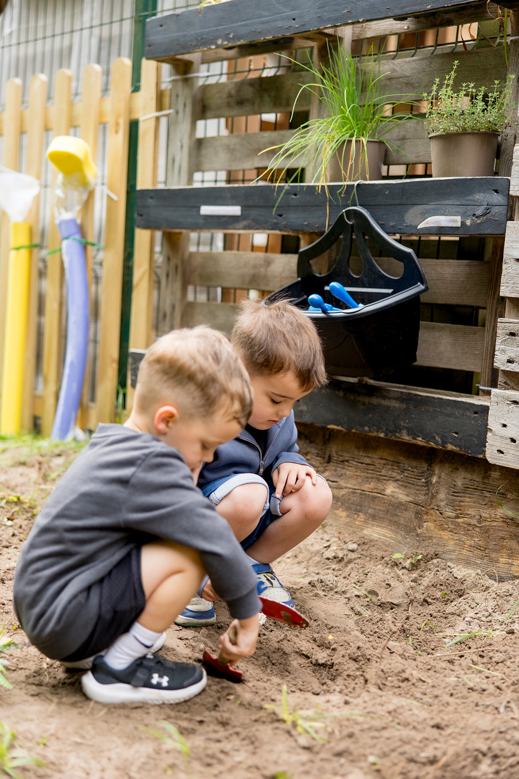 Two boys crouched down digging with trowels beside the planting beds