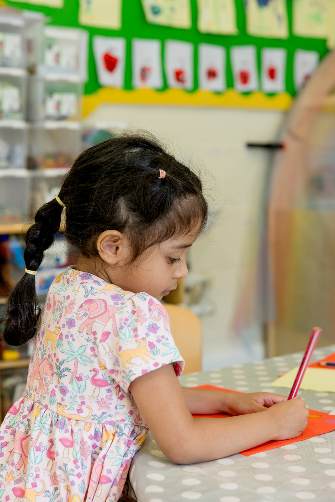A girl drawing carefully at the art table with a pot of pencils in front of her