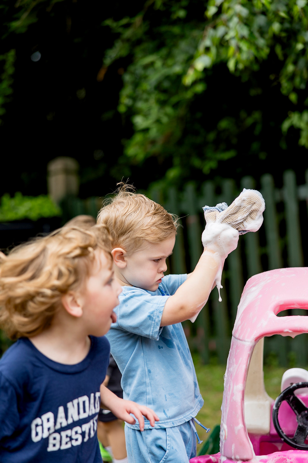 A boy studying a foamy washing mitt on his hand beside a pink toy car
