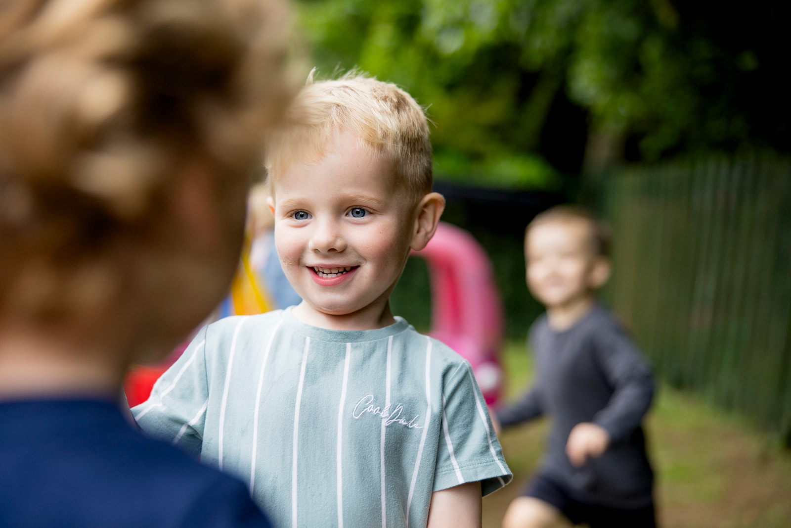 A smiling boy in the garden with children playing behind him
