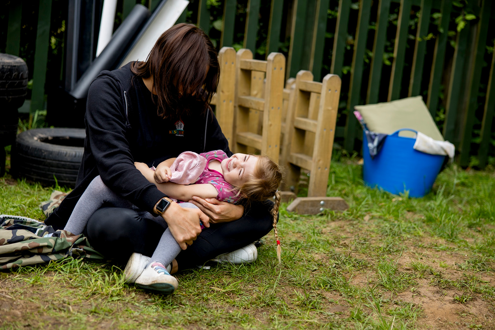 A staff member cuddling a laughing child on the grass in the garden