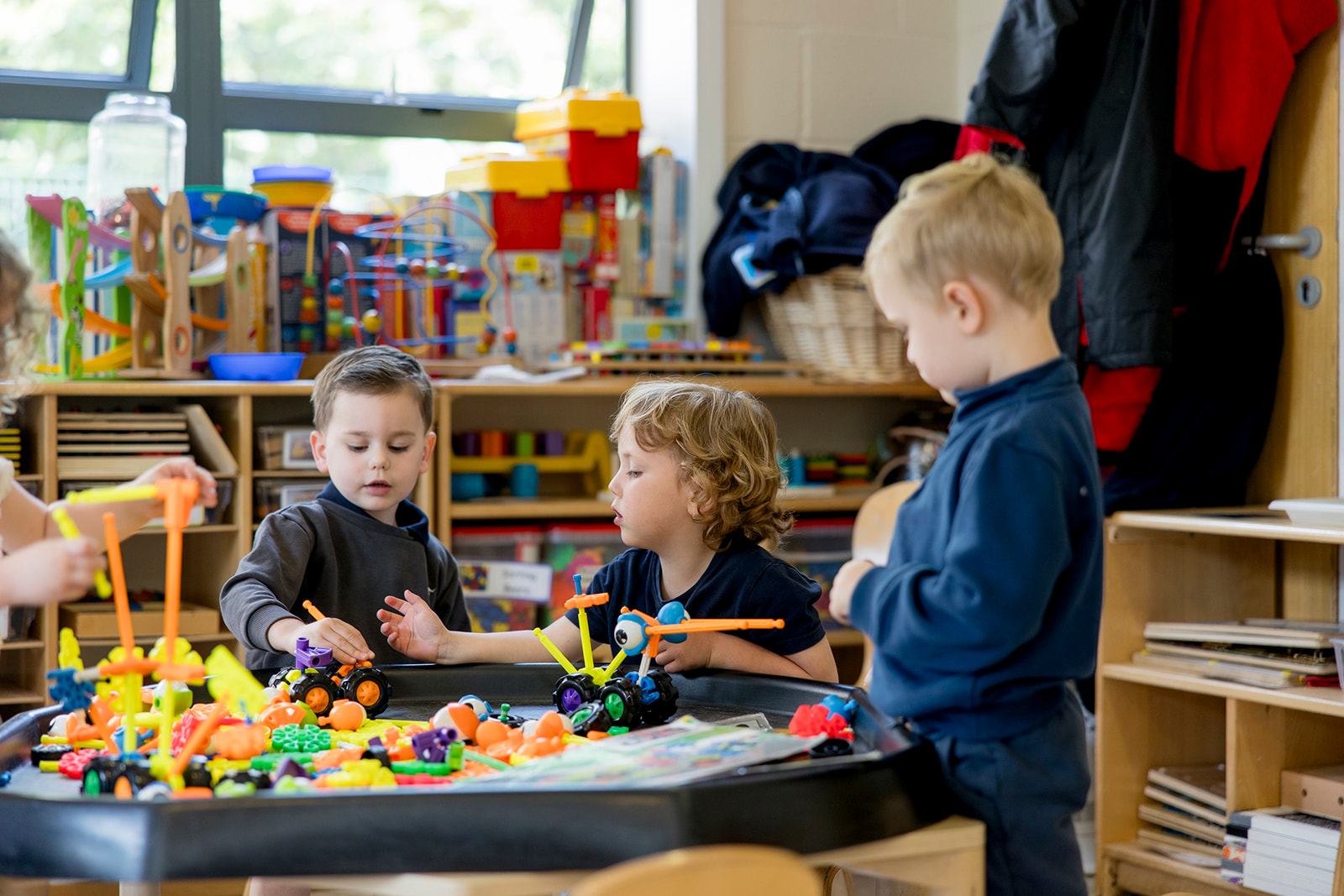 Three boys building with colourful construction toys at a tuff tray indoors