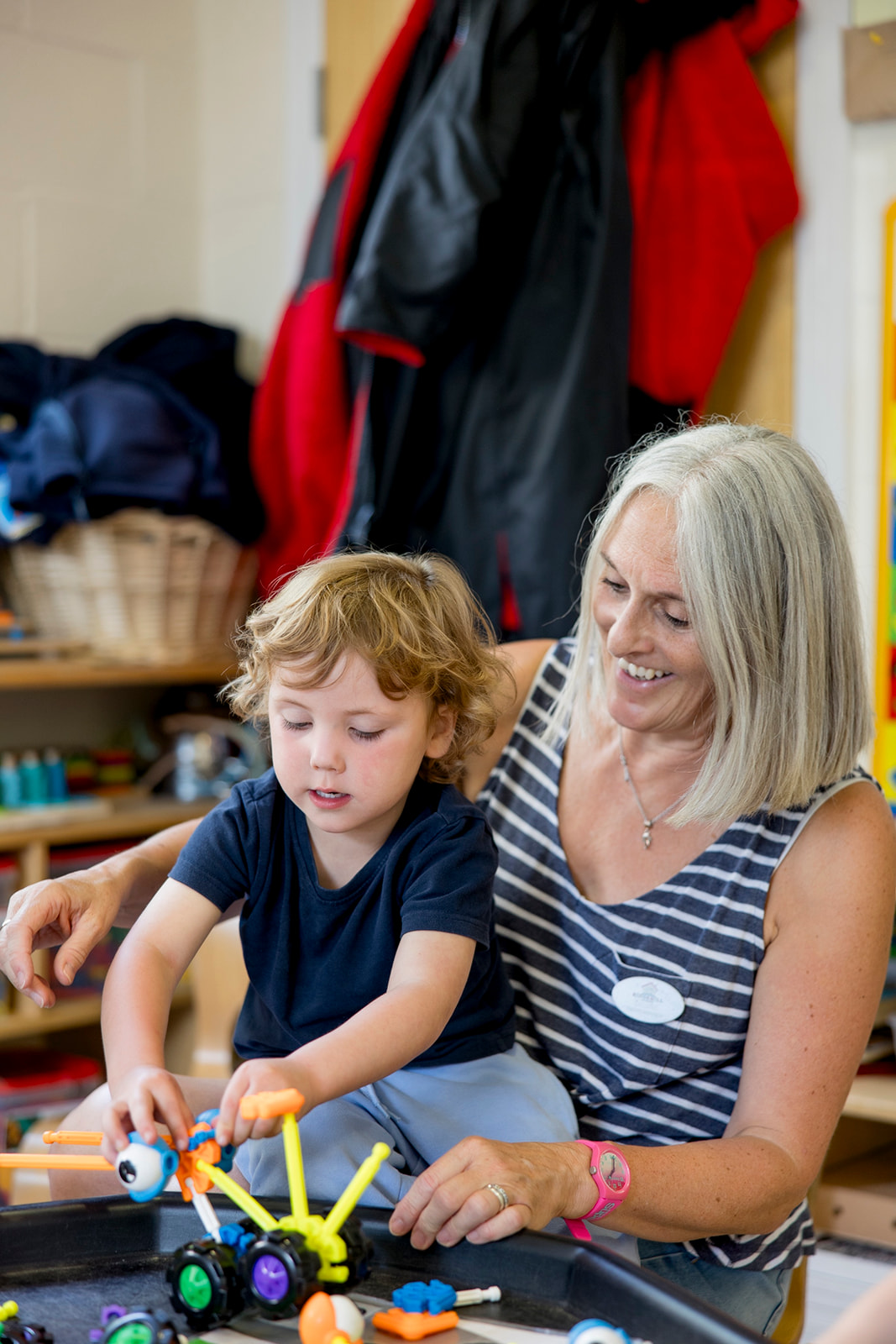 A staff member and child building with construction toys together at a tuff tray